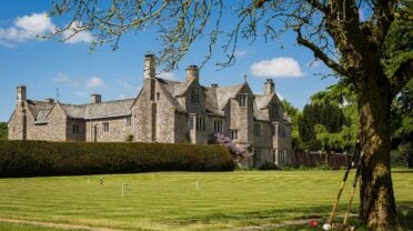 Cadhay, Devon – Stone country house viewed across manicured lawn with ancient oak tree in foreground.