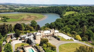Pentillie Castle, Cornwall – Aerial view of stone manor house with swimming pool and grounds overlooking river bend.