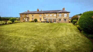 Greens Norton House, Northamptonshire – Stone country house with manicured lawn and hedged garden boundaries.