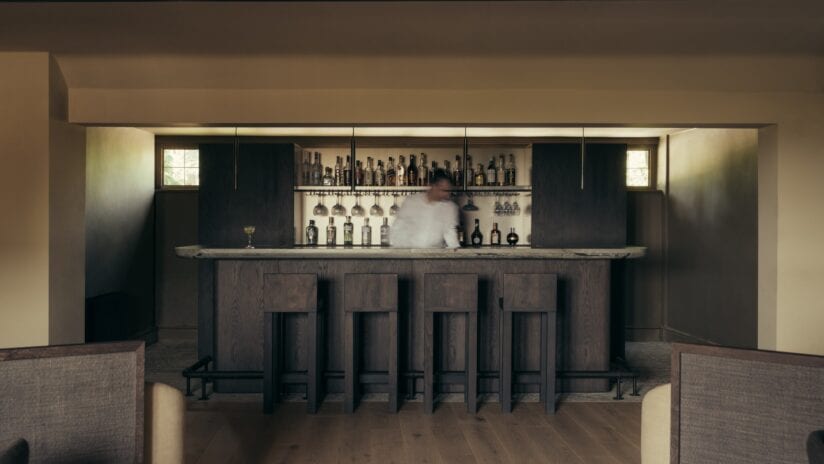 Hyll Hotel, Gloucestershire – Dark wood bar with shelving, pendant lights, and stone flooring.