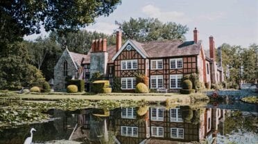 Brinsop Court – Tudor half-timbered manor reflected in pond with manicured topiary and chimney stacks