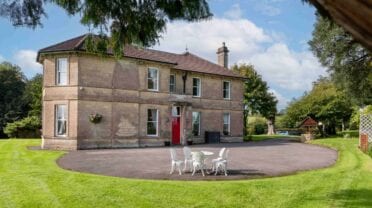 Cholwell Hall, Somerset – Stone country house with red front door and circular driveway, surrounded by mature gardens.