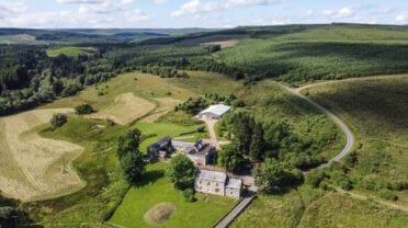 The Comb, Northumberland – Stone country house with modern extension set in moorland and forestry, aerial view.