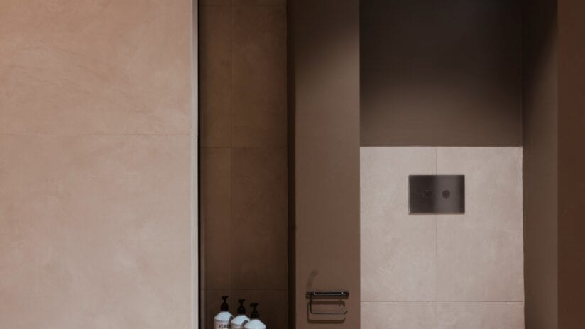 Hyll Hotel, Gloucestershire – Modern bathroom with beige tile walls, dark wooden niche shelving, and black light switch plate.
