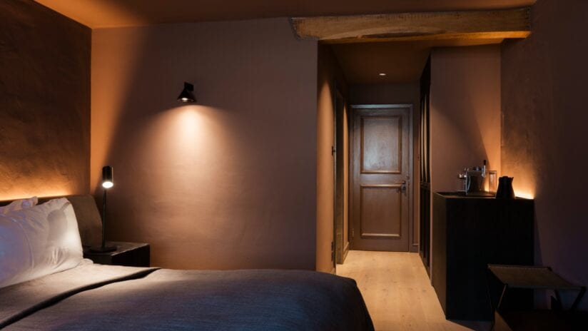 Hyll Hotel, Gloucestershire – Bedroom with exposed wooden beam ceiling and warm ambient lighting.