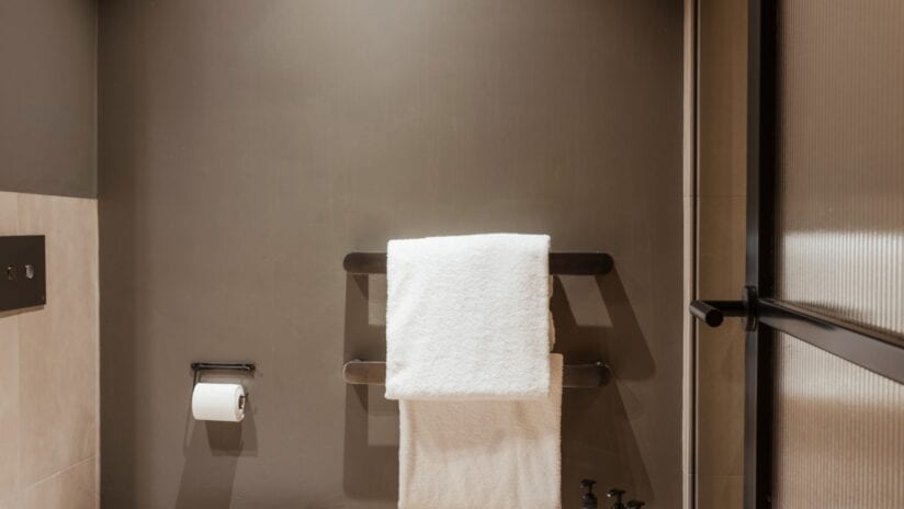 Hyll Hotel, Gloucestershire – Modern bathroom with heated towel rail and white towels against taupe walls.
