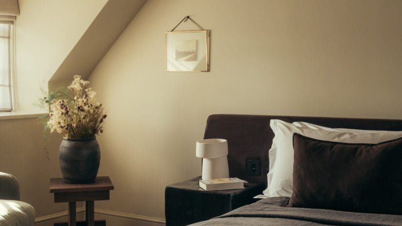 Hyll Hotel, Gloucestershire – Attic bedroom with sloped ceiling, dark headboard and dried flowers in ceramic vase.