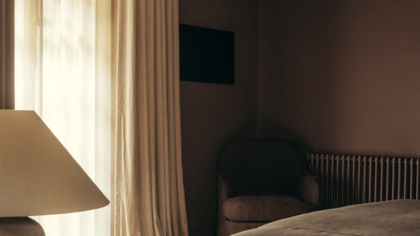 Hyll Hotel, Gloucestershire – Bedroom with beige curtains, bedside lamp, and wall-mounted television.