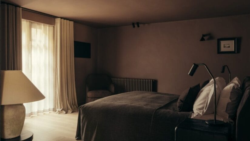 Hyll Hotel, Gloucestershire – Bedroom with brown velvet bed, cream curtains, and bedside lamp.
