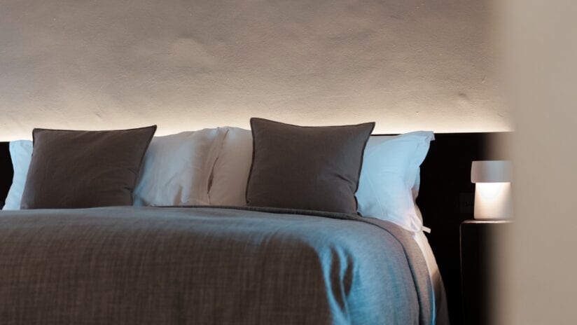 Hyll Hotel, Gloucestershire – Bed with layered pillows and blue linen bedding, bedside table with lamp.