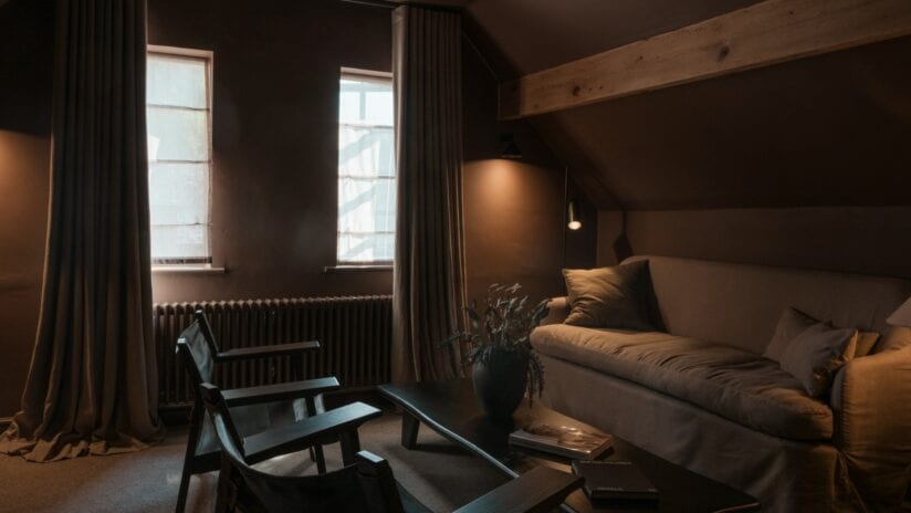Hyll Hotel, Gloucestershire – Dark modern bedroom with exposed wooden beams and floor-to-ceiling windows.
