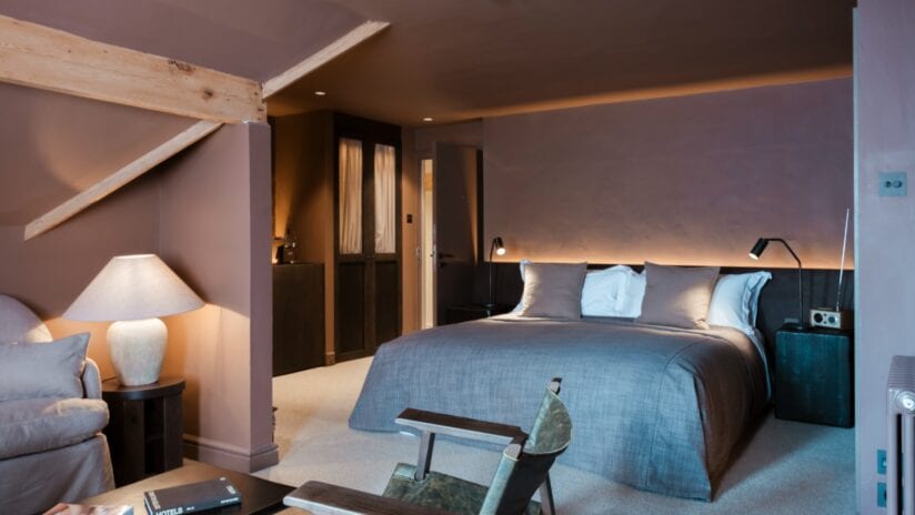 Hyll Hotel, Gloucestershire – Modern bedroom with exposed timber beam, blue upholstered bed, and ambient lighting.