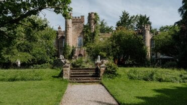 Augill Castle, Cumbria – Stone castle with crenellated towers viewed across manicured lawn and gravel approach.