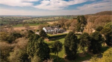 Holly House, Derbyshire – Aerial view of country house with ivy-covered trees and rolling valley farmland beyond.