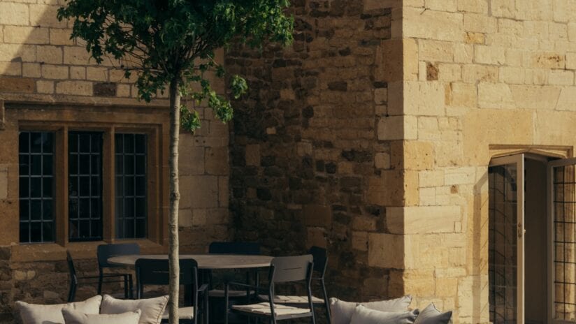 Hyll Hotel, Gloucestershire – Stone courtyard with climbing ivy, dining table and chairs, period windows.