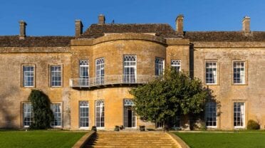 North Cadbury Court, Somerset – Stone country house facade with leaded windows, wrought-iron balcony and manicured lawn.