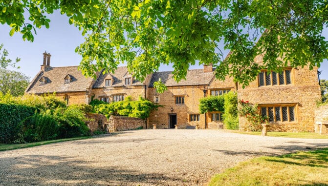 Tysoe Manor, Warwickshire – Stone manor house with mullioned windows and gravel driveway, shaded by mature trees.