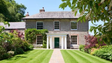 Gitcombe House, Devon – Stone Georgian house with white portico, manicured lawn, and flowering shrubs.