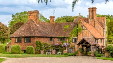 Burrow Farm Estate, Buckinghamshire – Red brick manor house with multiple chimneys, ivy-covered walls, and manicured topiary beside gravel drive.