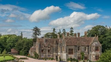 Huntsham Court – Stone country house with crenellated roofline and chimneys, surrounded by mature trees