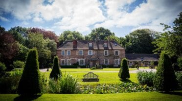 Solton Manor Estate, Kent – Brick manor house with manicured grounds, topiary conifers and wooden bench.