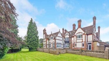 Kingswood Manor, Surrey – Tudor-style country house with brick and half-timber façade, tall chimneys, and manicured lawns.