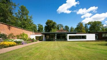 Leuchie Walled Garden – Modern single-storey extension with large windows and manicured lawn bordered by flowering beds