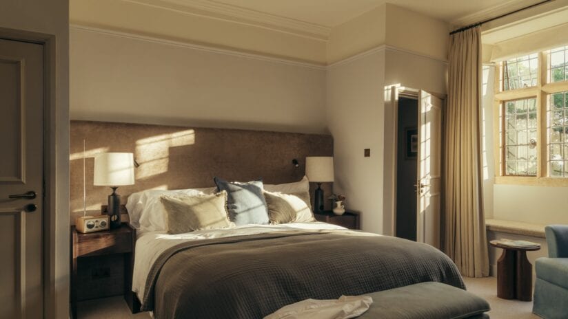 Hyll Hotel, Gloucestershire – Master bedroom with upholstered headboard, wooden bedside tables, and tall sash windows.