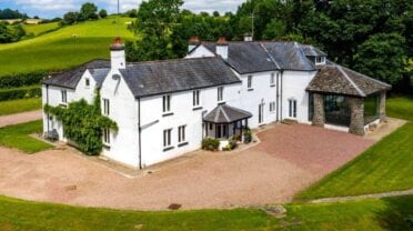 Monnow Valley Studio, Monmouthshire – White rendered country house with slate roof and gravel driveway surrounded by rolling green fields.