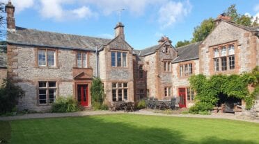 Morland House, Cumbria – Stone and red-brick country house with slate roof, manicured lawn, and patio seating area.