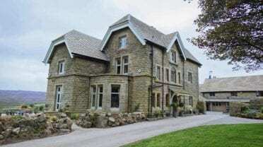 Moscar Lodge – Victorian stone mansion with slate roof and manicured grounds overlooking moorland valley