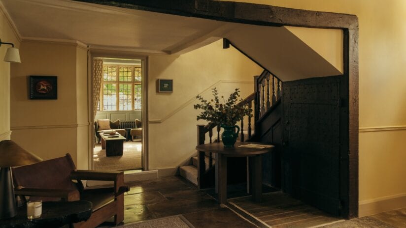 Hyll Hotel, Gloucestershire – Hallway with wooden staircase, exposed beam, and cream-painted walls with period features.
