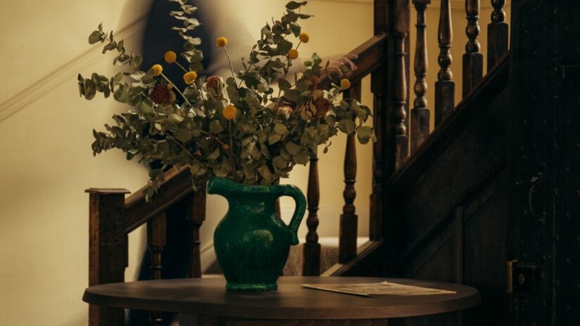 Hyll Hotel, Gloucestershire – Curved wooden console table with green ceramic pitcher and dried flowers on staircase landing.