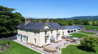 Tatham House, Somerset – Cream-rendered country house with slate roof and chimneys, manicured lawns and valley views.
