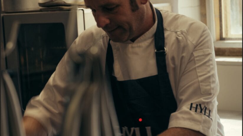 Hyll Hotel, Gloucestershire – Chef preparing food in kitchen with Aga cooker and stainless steel appliances.