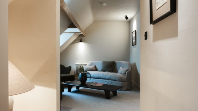 Hyll Hotel, Gloucestershire – Attic sitting room with sloped ceiling, grey sofa and black coffee table.