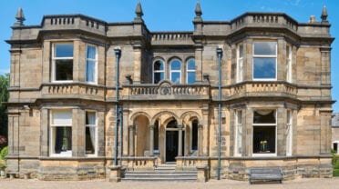 Stretton House, Derbyshire – Ashlar stone country house with castellated roofline, arched windows and central entrance portico.